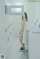 A naked woman standing in front of a washing machine.