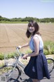 A woman standing next to a bike in a field.